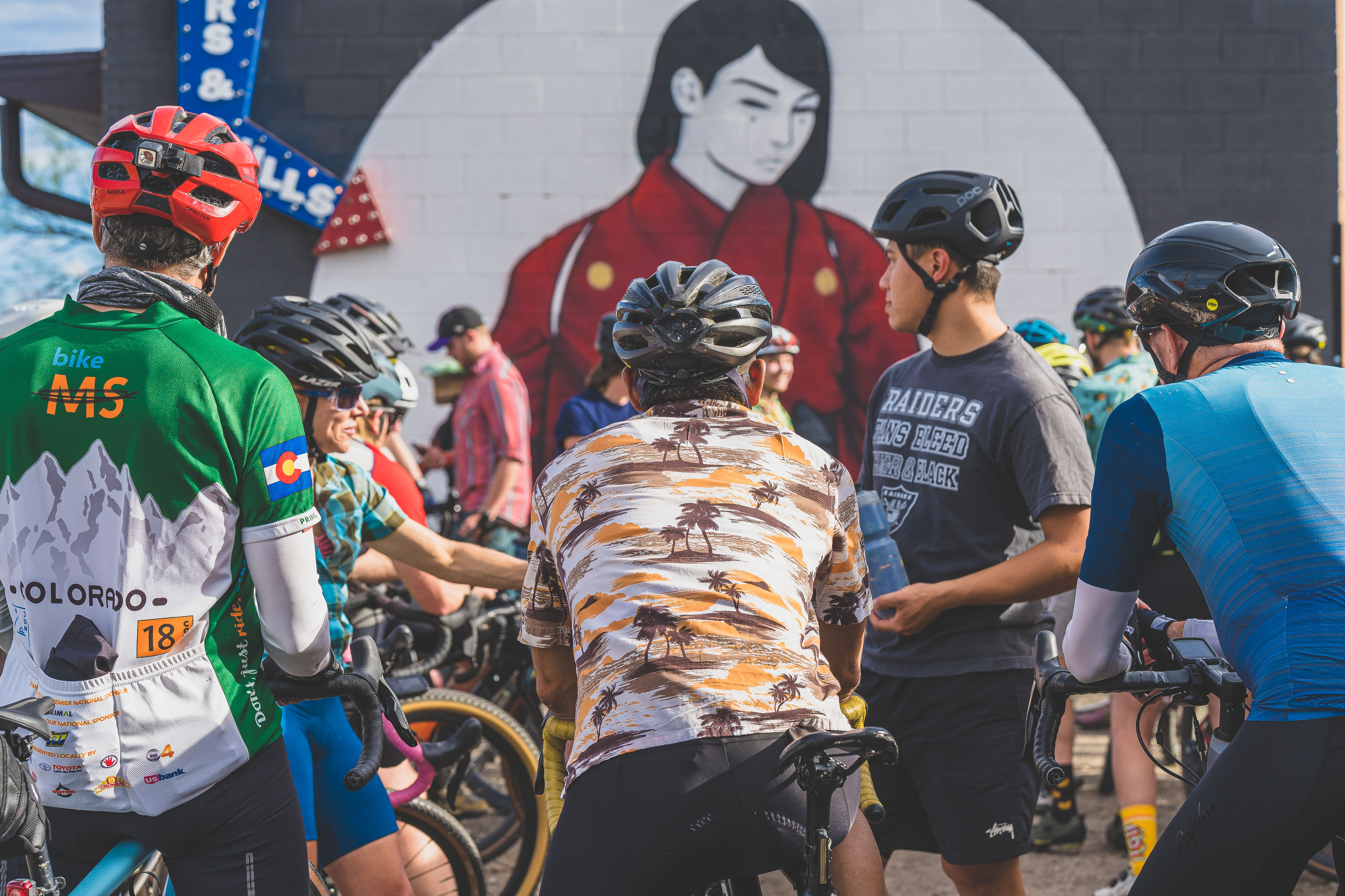 Cyclists gathered together with their bikes in front of a mural